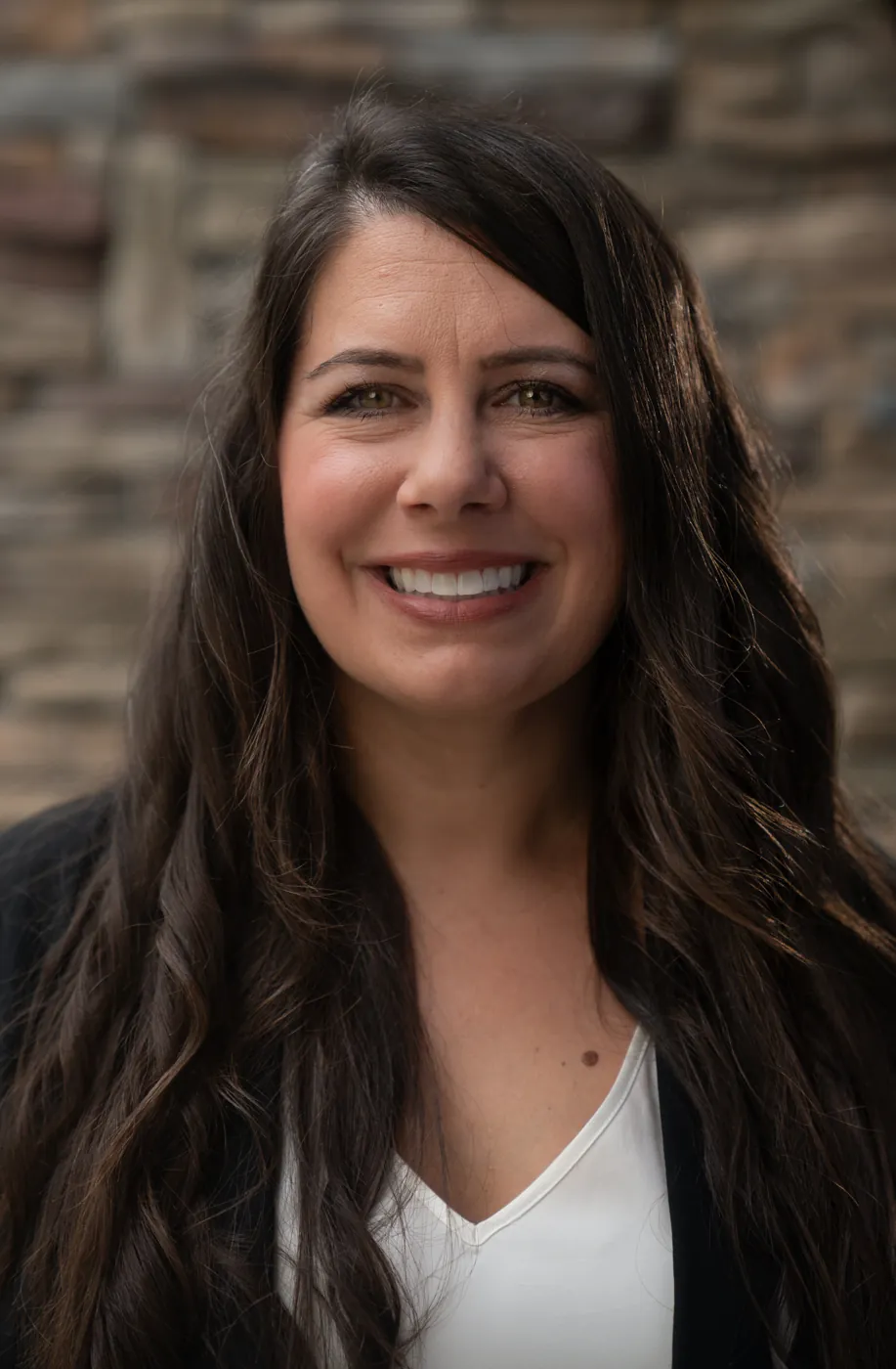 Professional headshot of a smiling woman against a brick wall