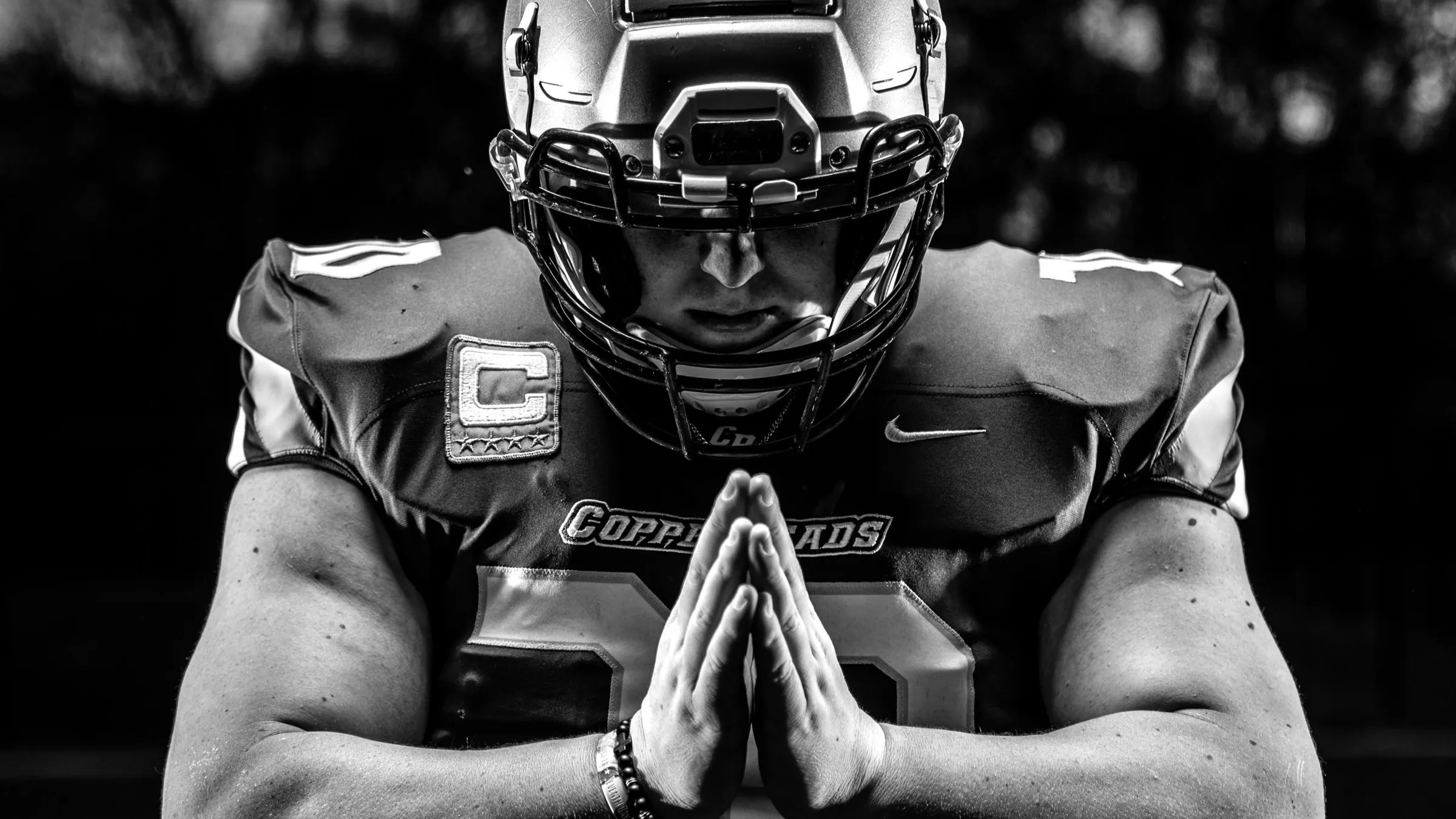 Football player in black and white, hands pressed together, lit from above