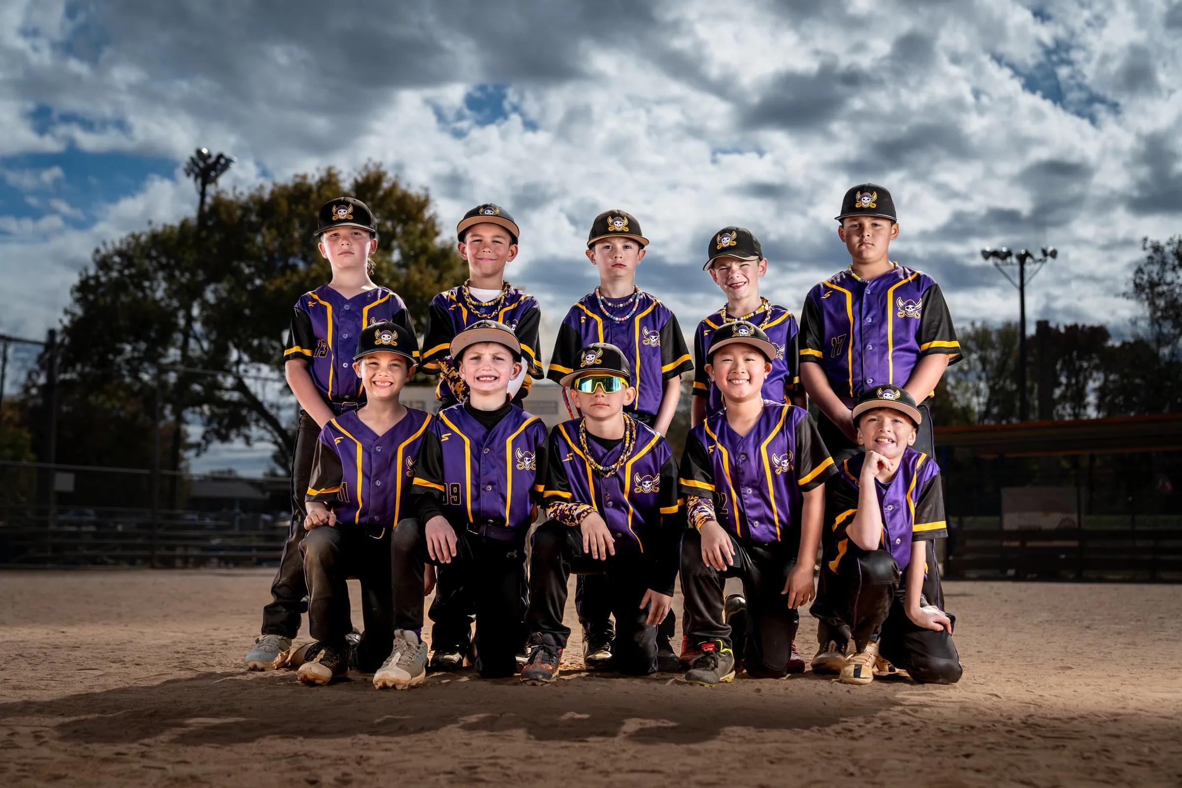 Youth baseball team posed together on the infield under a cloudy sky